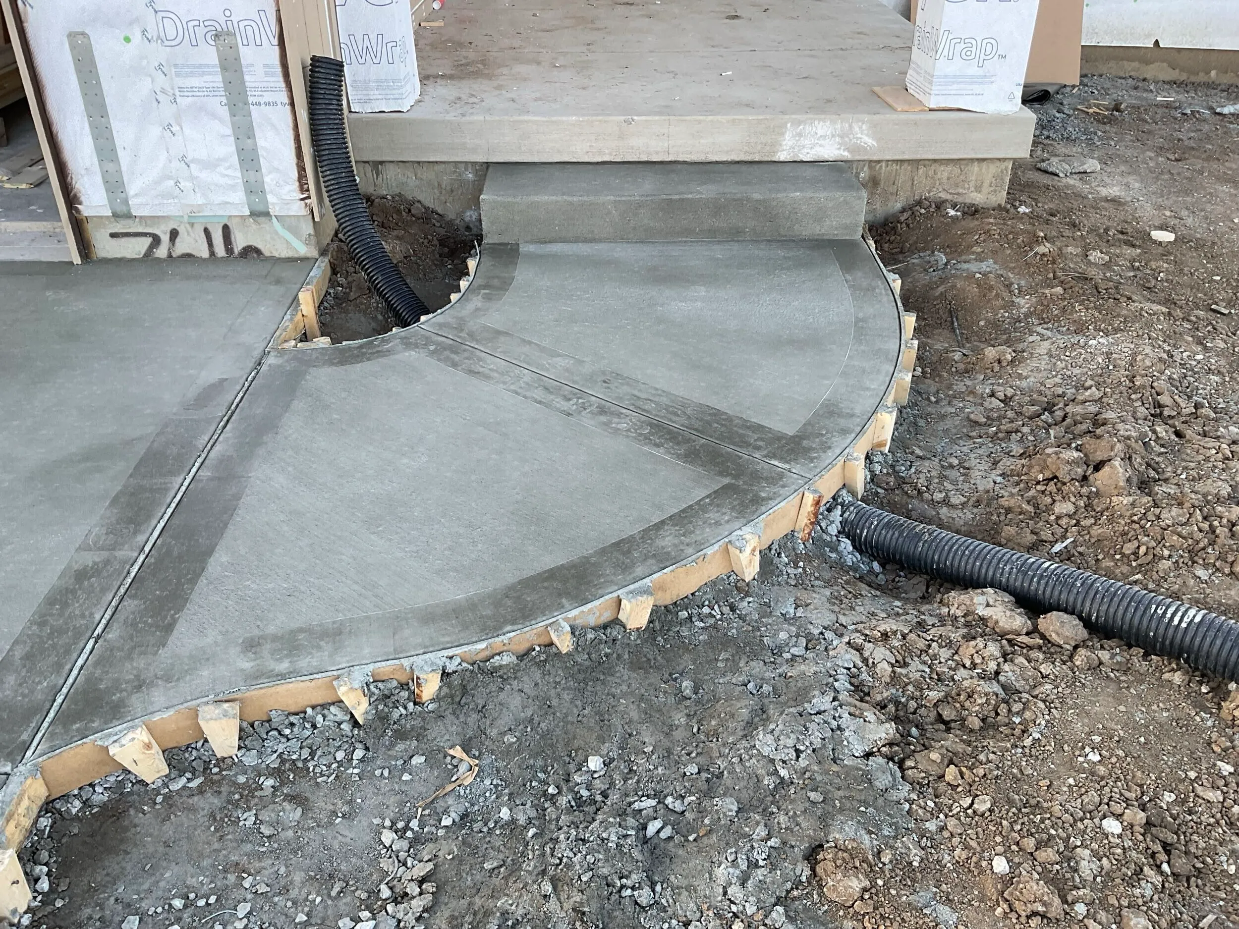 Curved concrete walkway and step pad next to a new build
