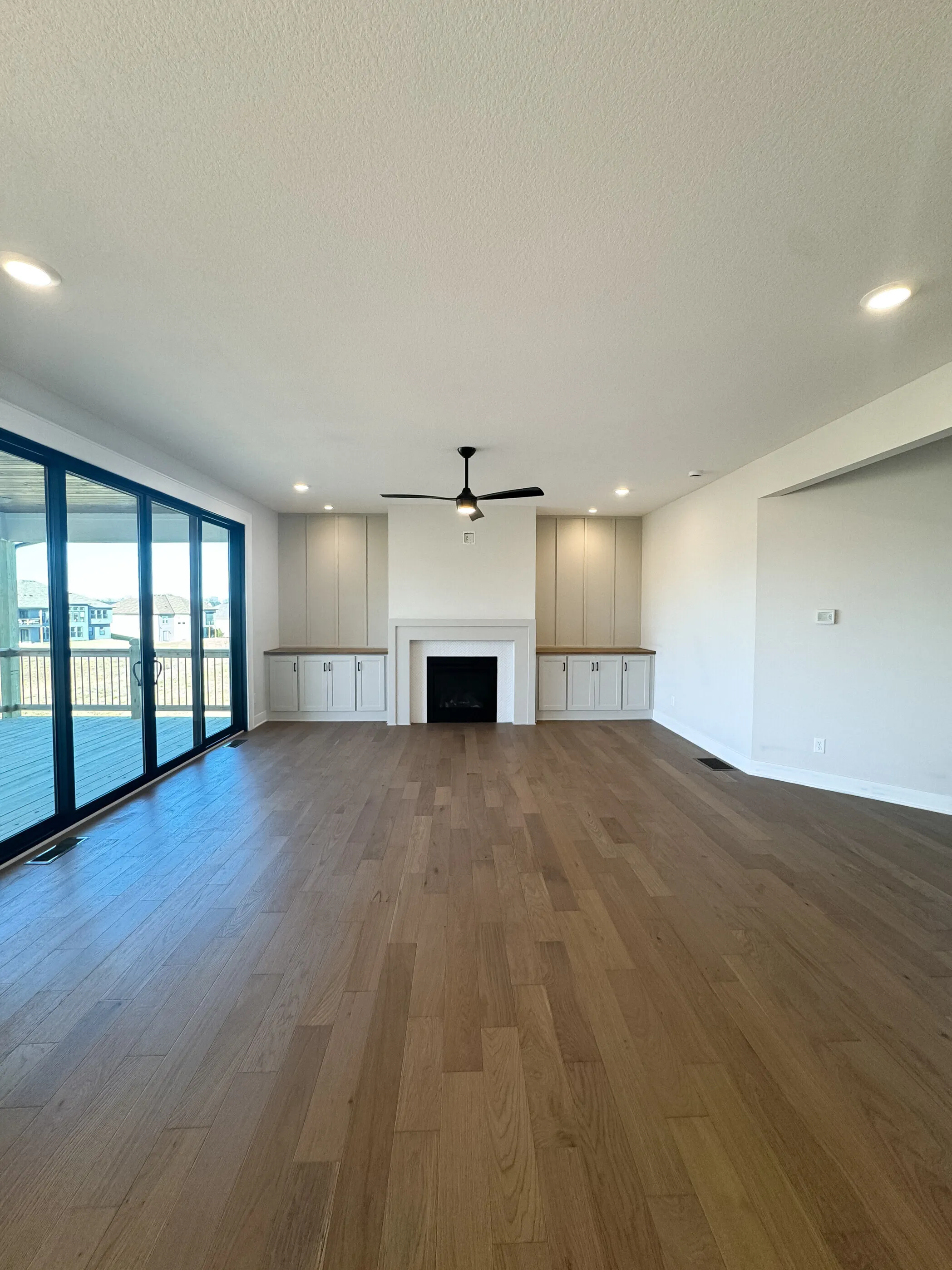 Open-concept living room with fireplace, white built-ins, four-panel slider, and wide-plank hardwood floor